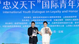 Li Zijun (right), a scholar of the Chinese Theatre Literature Society, displays a photo of his grandfather, Li Hongchun, portraying the legendary Chinese figure Guan Gong during the International Youth Dialogue on Loyalty and Honor Without Borders in Yuncheng, Shanxi province, on Wednesday. [Photo by Zhu Xingxin/China Daily]
